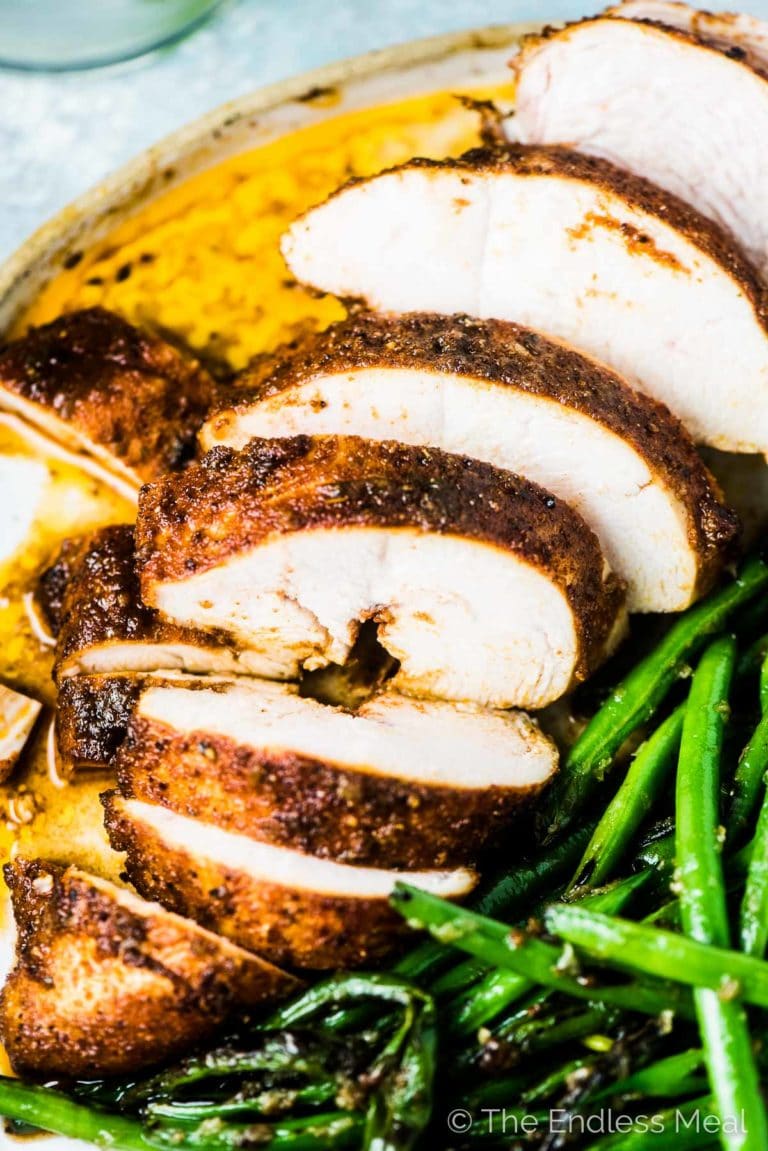 Close-up of a perfectly grilled chicken breast cut into slices with green beans on the side.