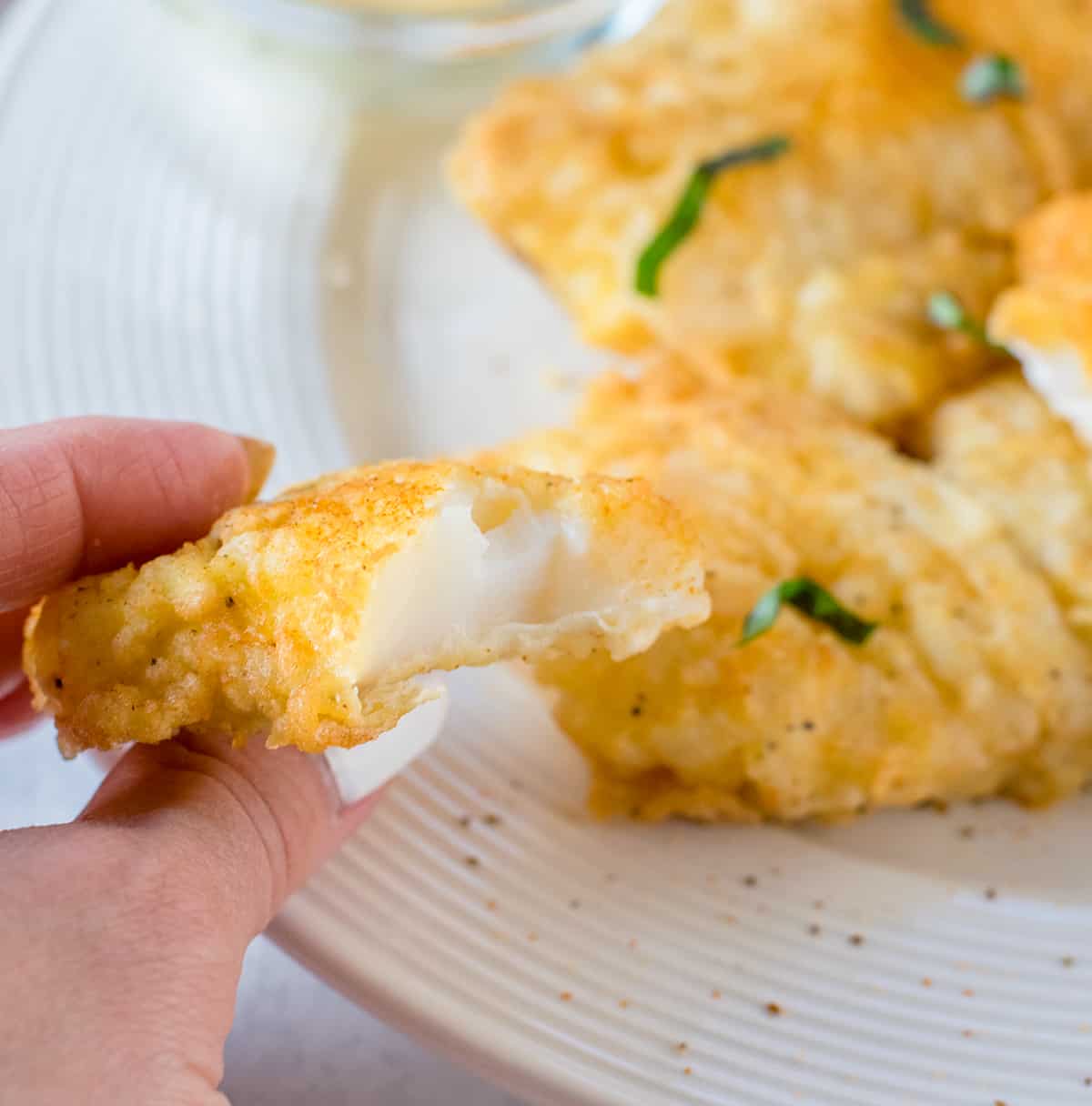 holding a piece of deep-fried cod
