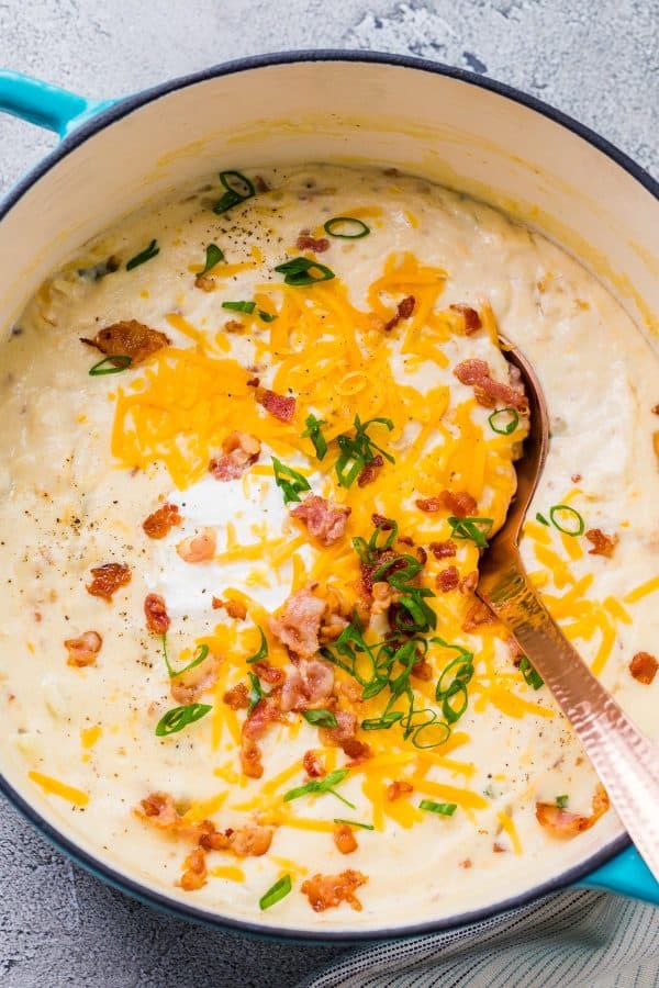 Potato soup made of potatoes, bacon and cheese in a Dutch oven with ladle and topped with greens and cheese.