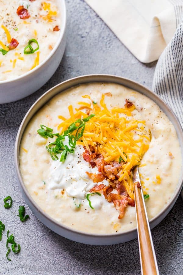 Top two bowls of soup with a spoon and topped with potato soup.