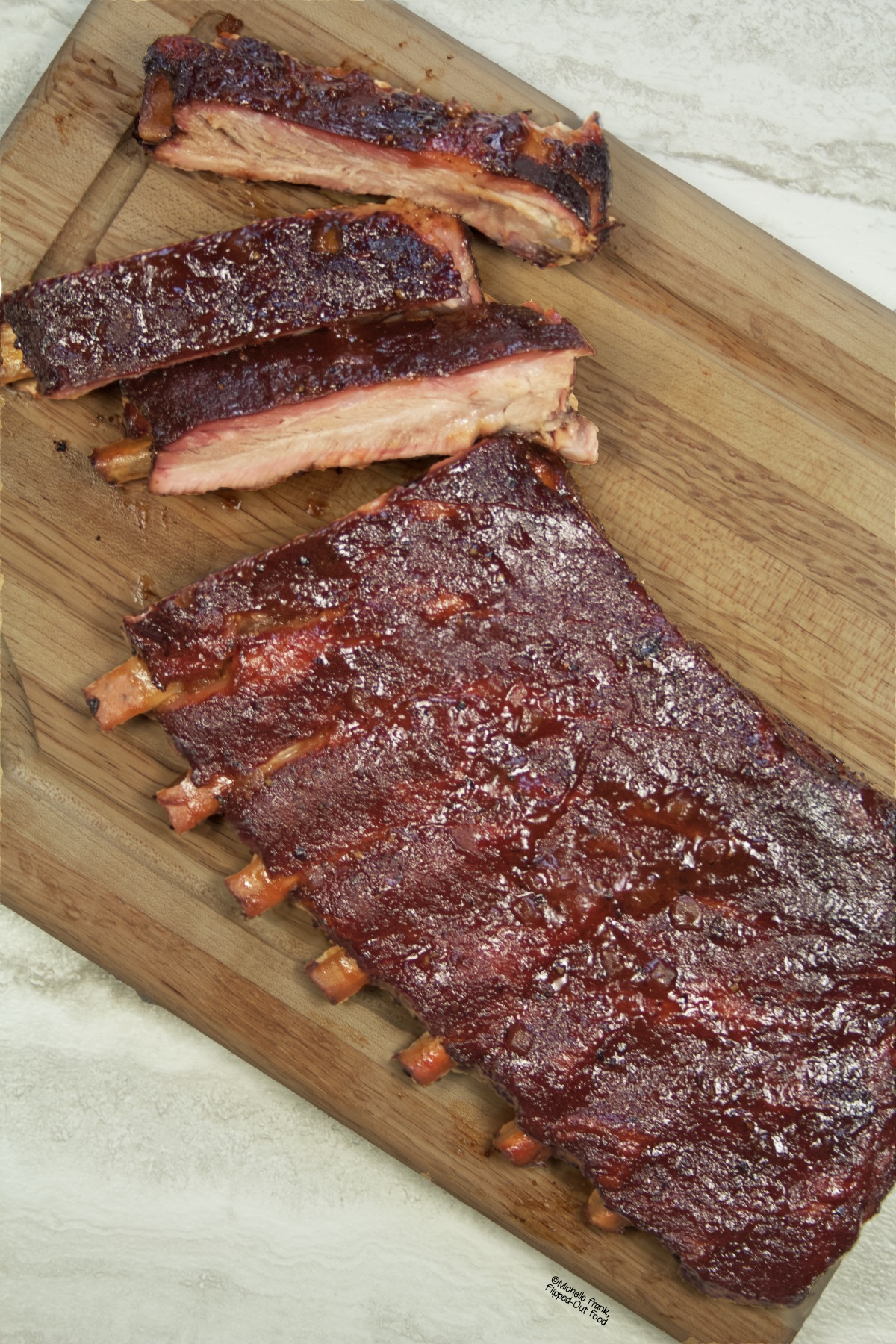 Side view of a partially cut rack of ribs that have been smoked on a charcoal grill, positioned on a cutting board