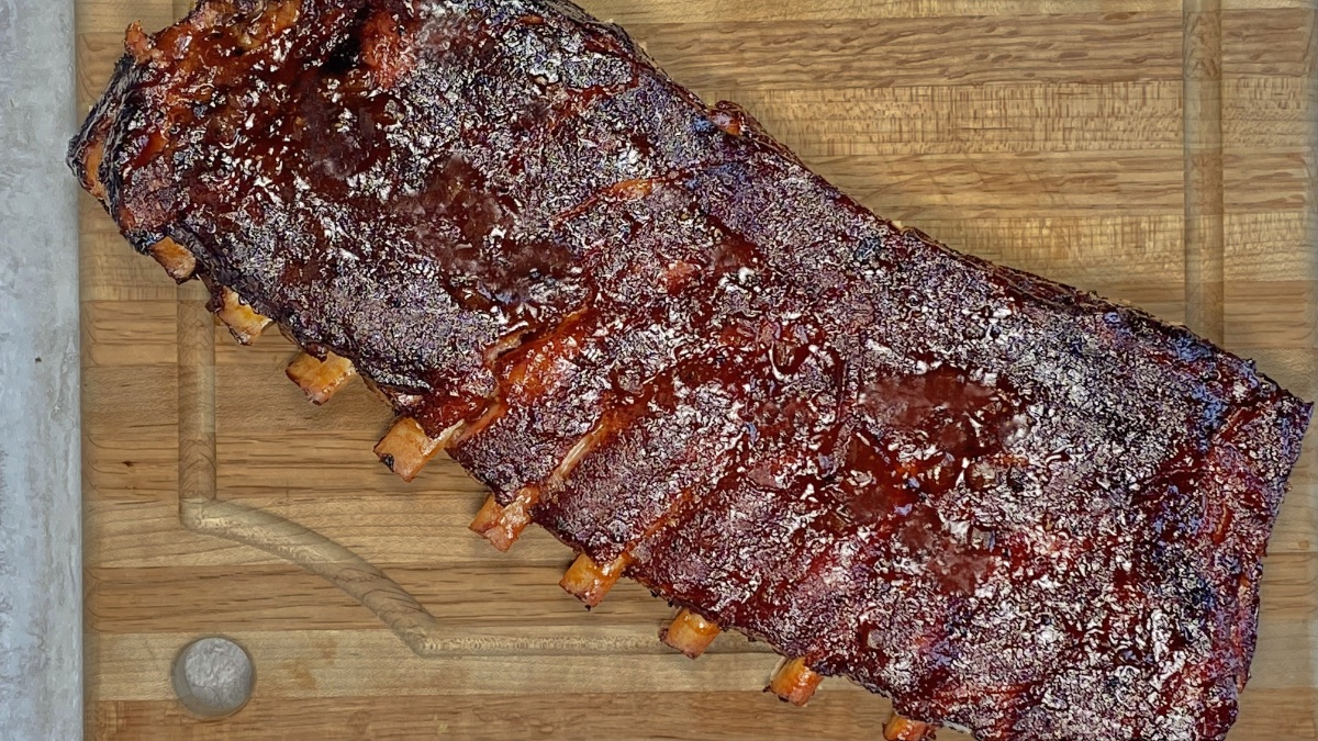 A rack of St. Louis ribs smoked on a charcoal grill, with meat pulling back nicely from the bone.