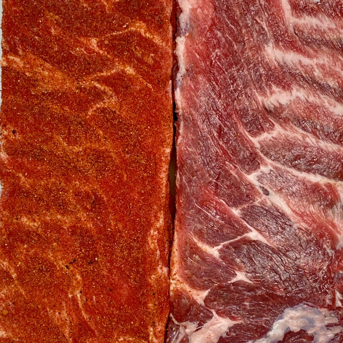 Overhead close up view of two racks of ribs side by side. One on the left rubbed down with rib rub, the one on the right, not rubbed yet.