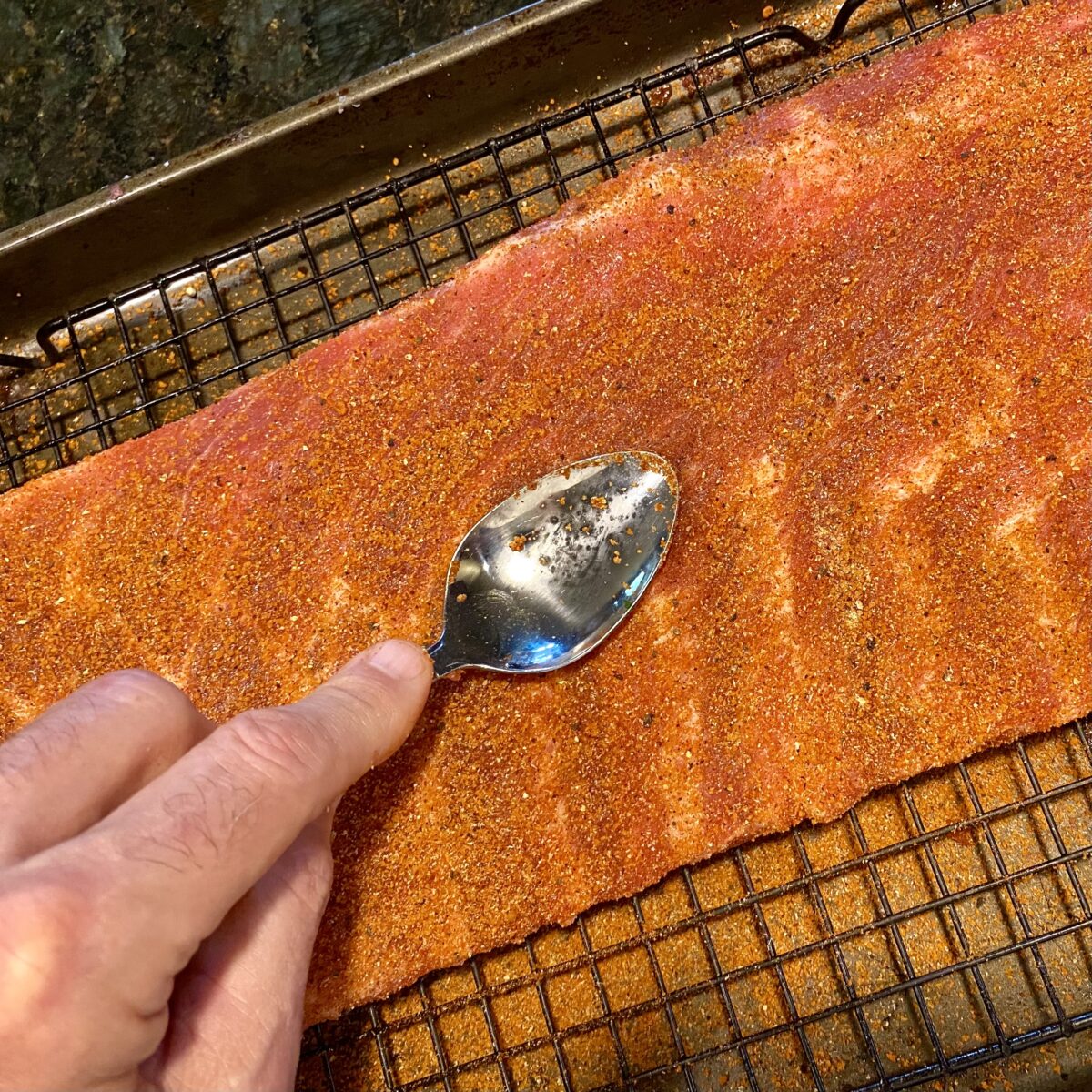 Top view showing how to use the back of a spoon to work the rib rub into the ribs.