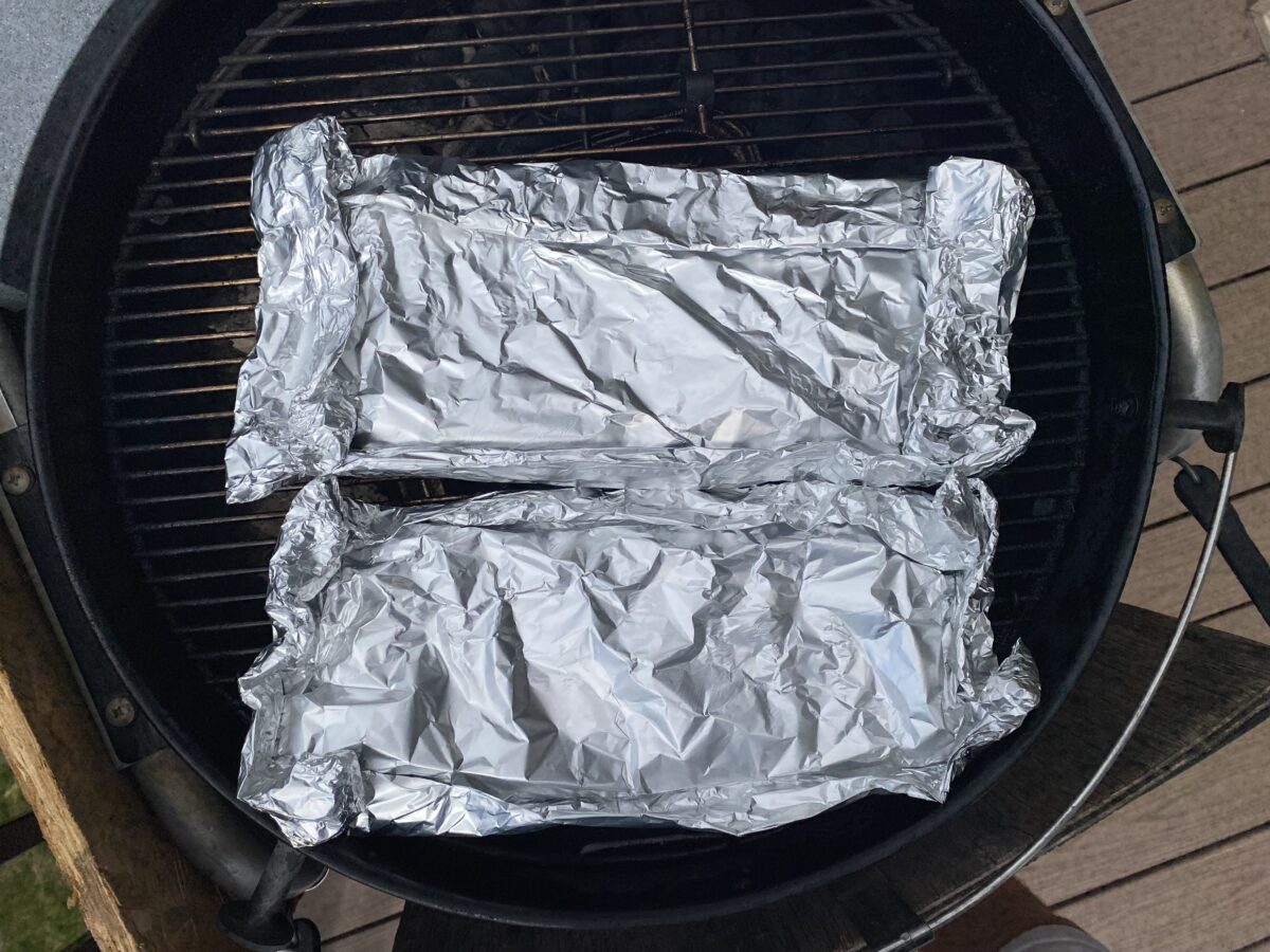 Overhead view of two racks of wrapped ribs on the charcoal grill.