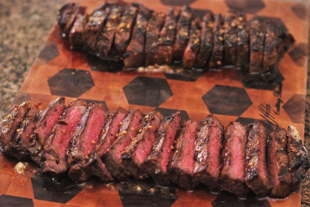 Two New York Strip Steaks grilled and sliced ​​on a wooden cutting board.