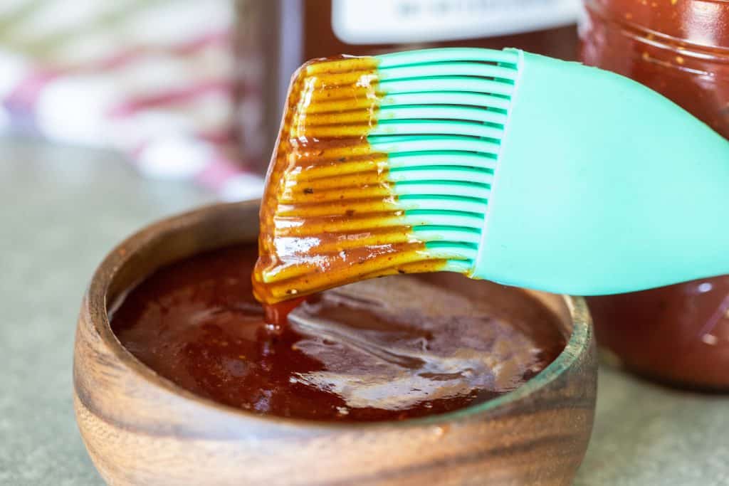 Mint broom dipped in a small wooden bowl filled with honey barbecue sauce.