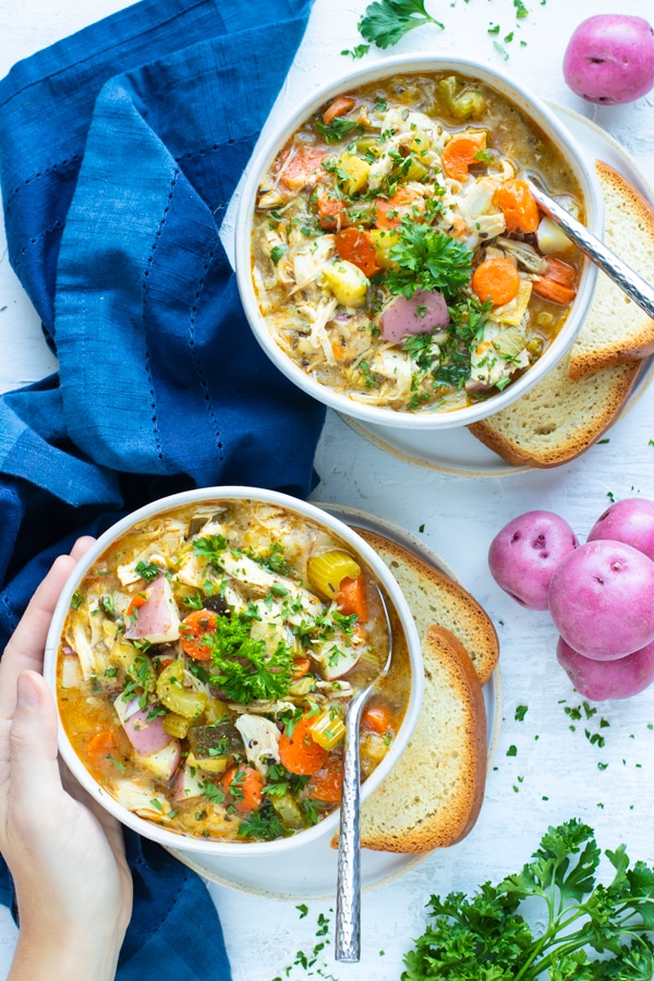 Two white bowls with blue napkins filled with chicken and vegetable soup recipes made in the Instant Pot.