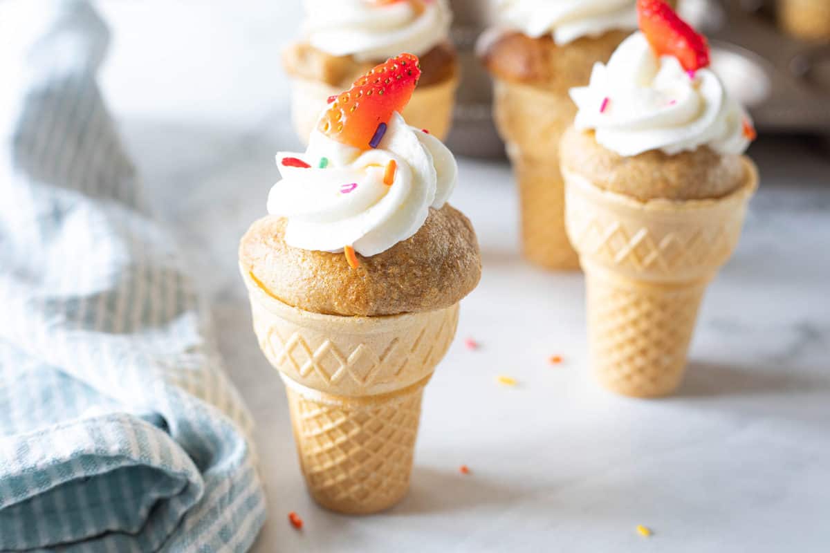 Ice cream cone cupcakes topped with almond butter cream, sprinkles and a slice of strawberry.