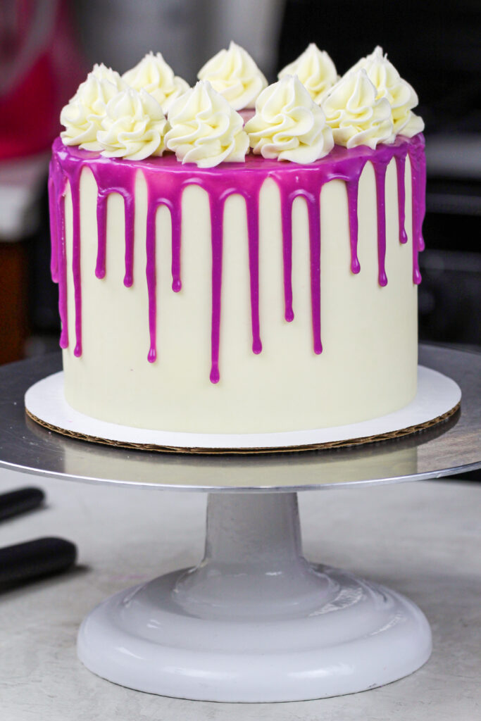 image of dripping white chocolate drops added to a cold buttercream cake to form a purple drip cake