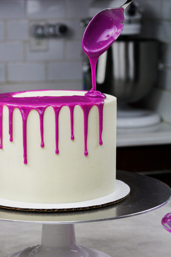 Image of white choc ganache drops added to a cold buttercream cake to create a purple drip cake