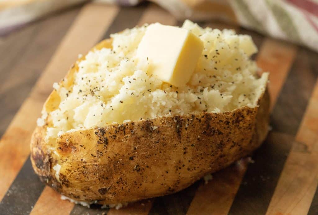 a block of butter on an open baked potato on a wooden cutting board