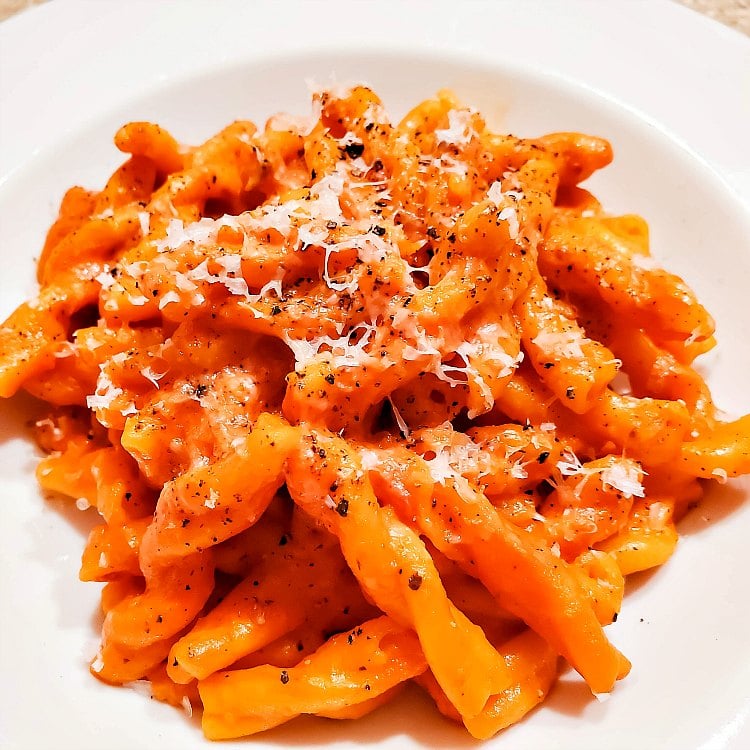 A plate of rotini pasta topped with sauce and topped with Parmesan cheese and black pepper.