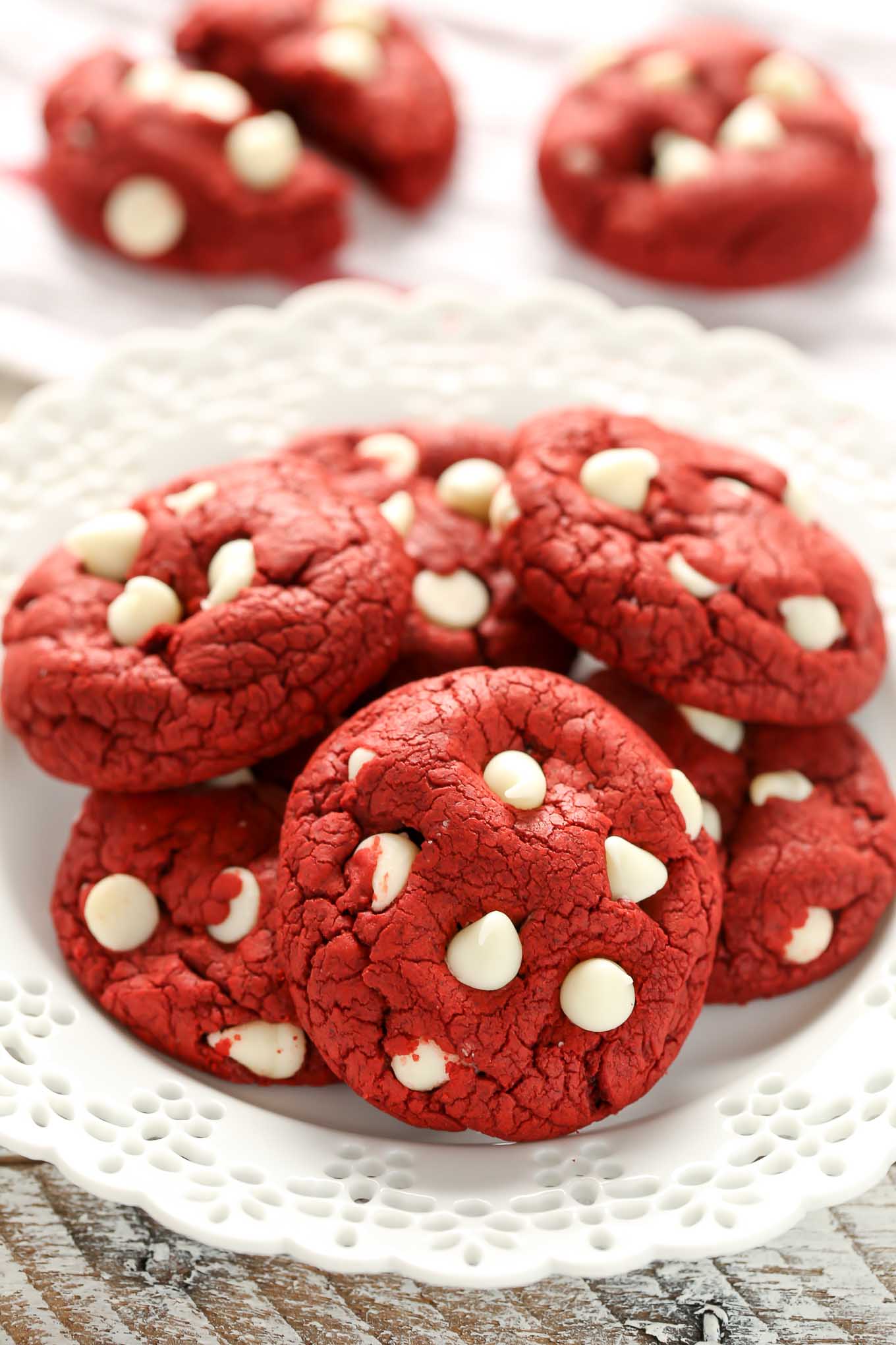 A white plate stacked with red velvet cookies. Two additional cookies are in the background.