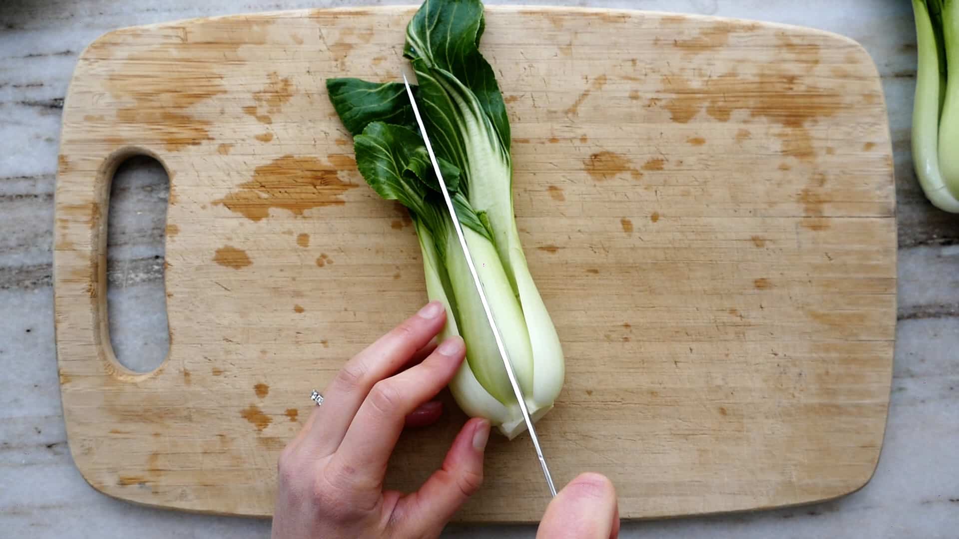 woman cutting bok choy in half on cutting board