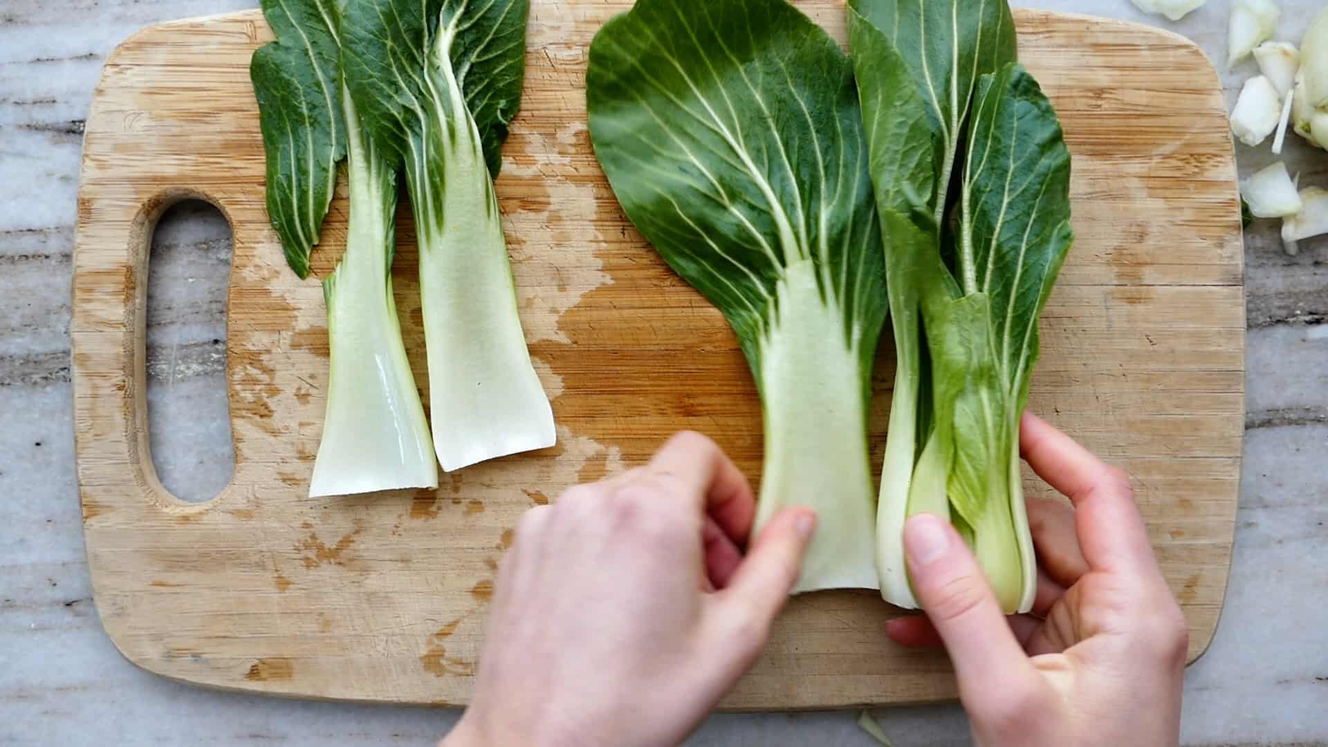 Woman pulling leaves from a head of a broccoli plant on a cutting board