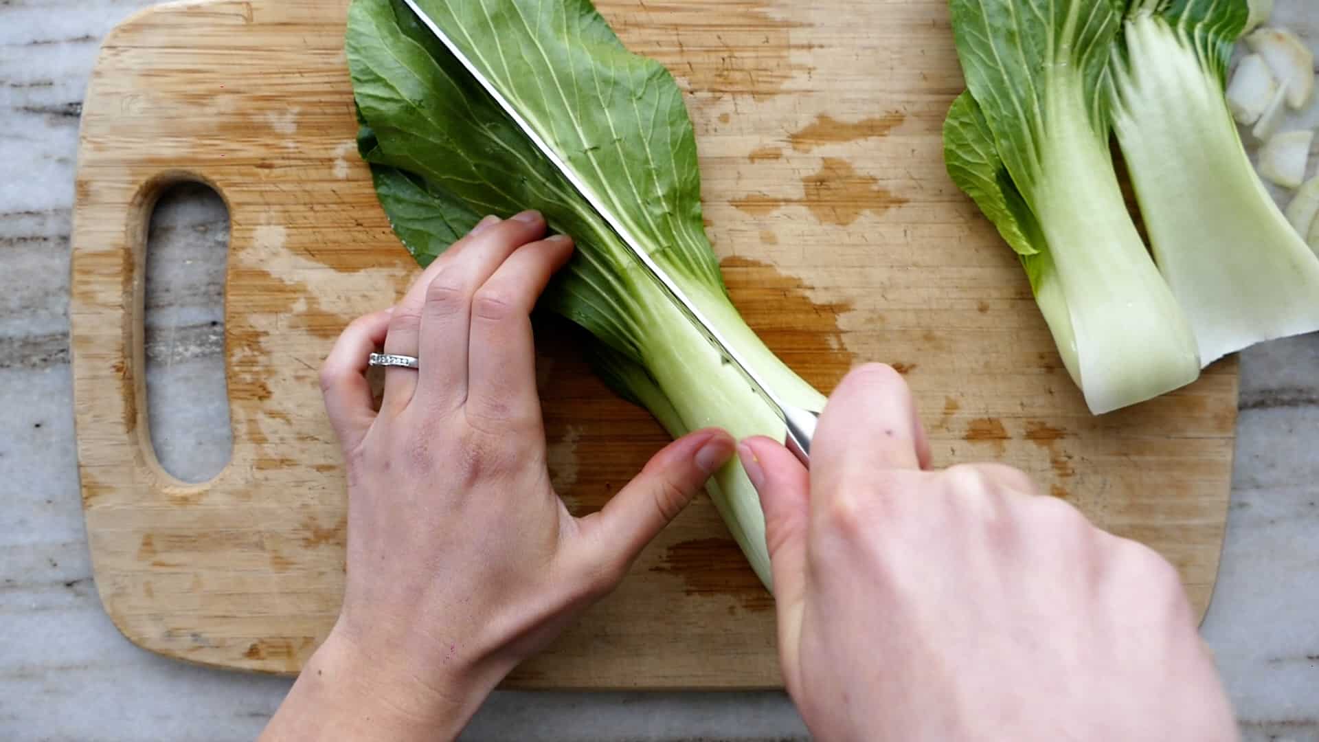woman slicing broccoli leaves lengthwise on cutting board