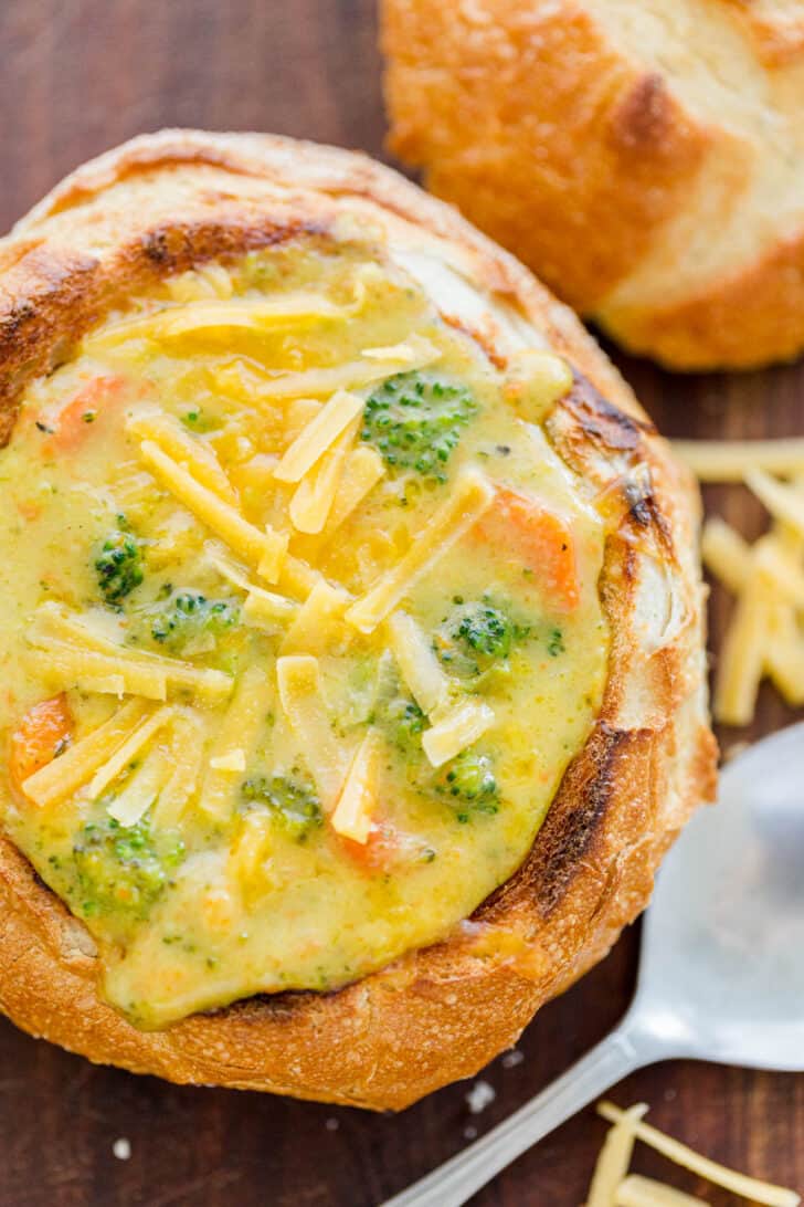 Broccoli cheese soup served in a bread bowl and topped with shredded cheddar cheese