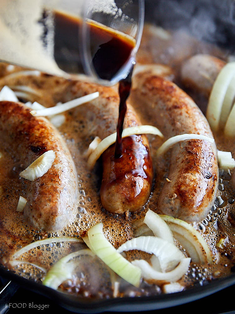 Brats cooked in beer with onions on the stove.