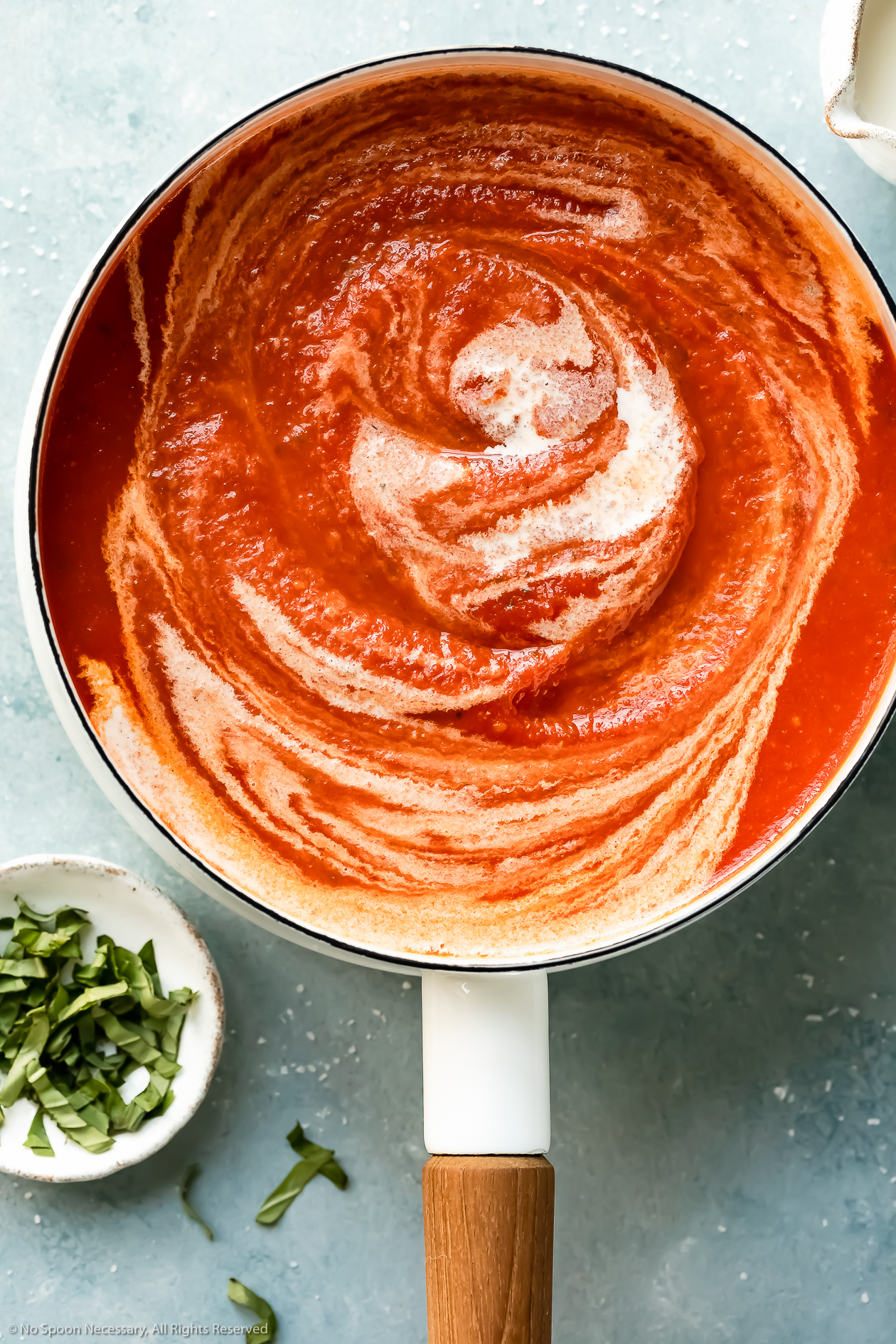Up-close angled photo of creamy homemade vodka sauce in a white saucepan with a black ladle lifting some of the sauce out of the pan.