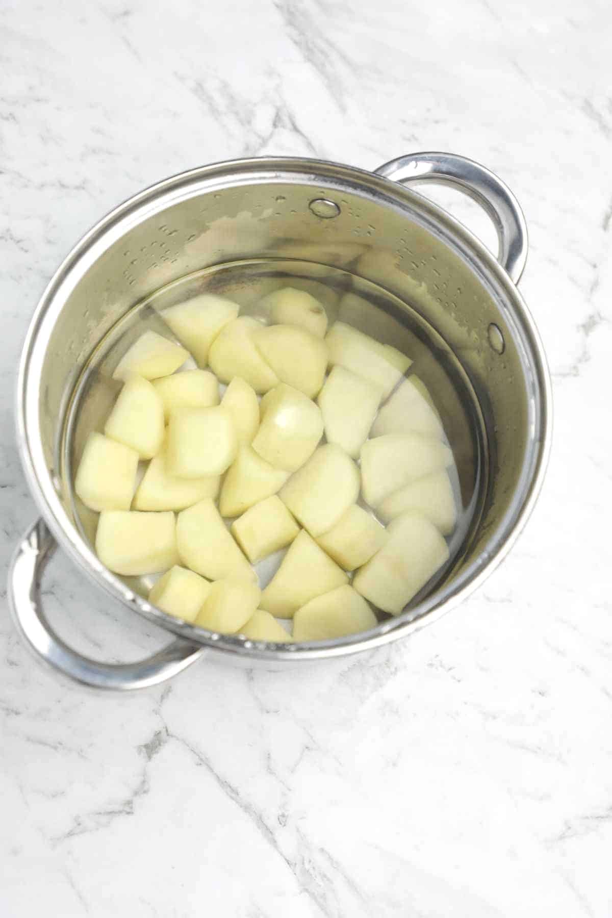 Potatoes soaked in water in a pot.