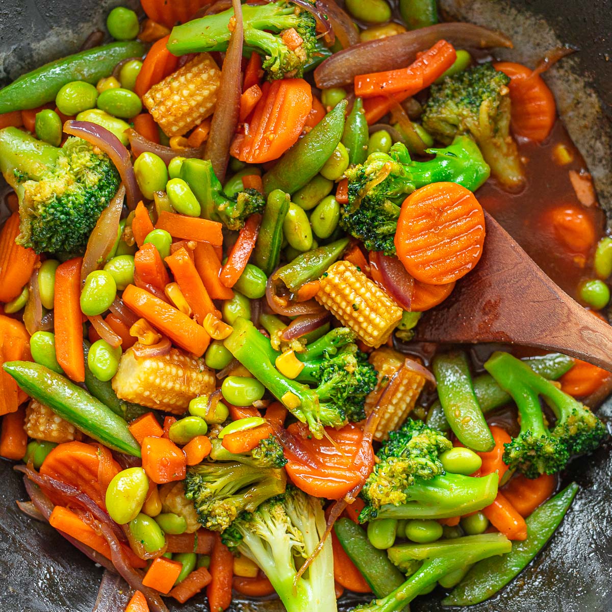 Stir-fry frozen vegetable mix in a pan, add shredded carrots, broccoli, baby corn, and peas.