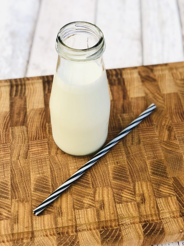 glass bottle filled with homemade pistachio ice cream milkshake with black and white striped reusable straw is on the board next to it