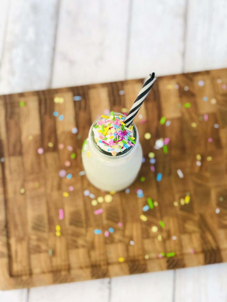 homemade pistachio ice cream shake a glass bottle covered with squirrel ice cream and sprinkle with unicorns, reusable straws with black and white stripes in the bottle and unicorns sprinkled all over the table