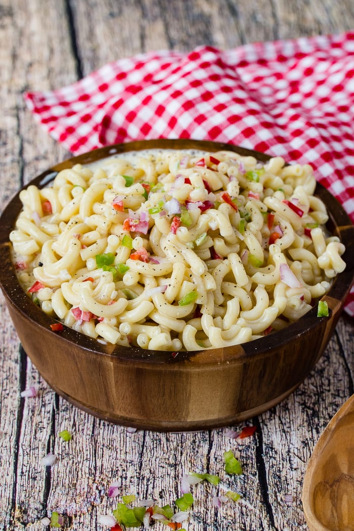 A wooden bowl on a red and white checkered napkin is filled with a creamy pasta salad.