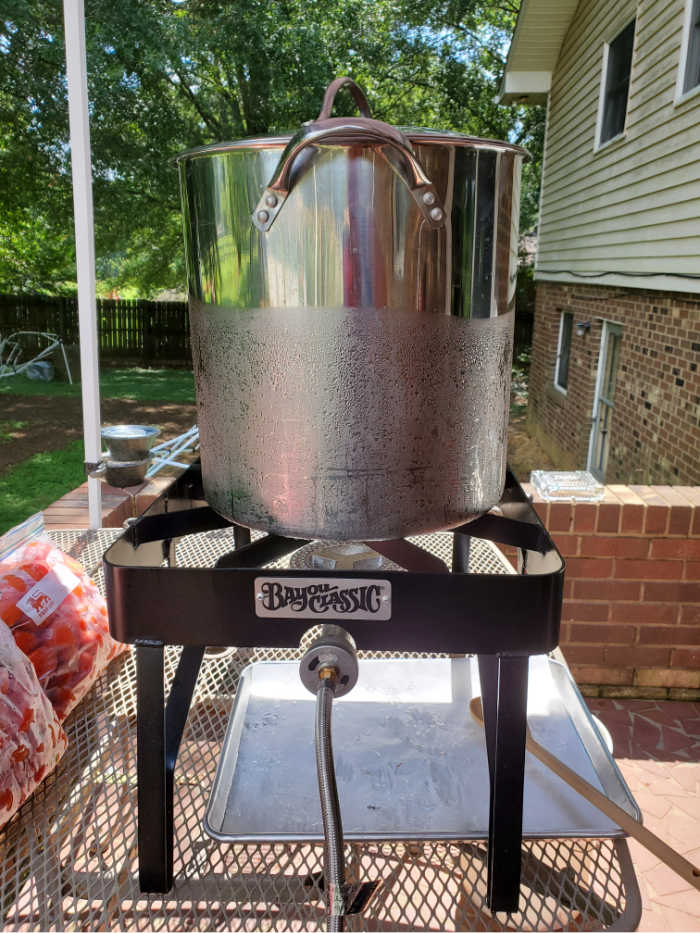 Outdoor burner with large storage kettle on outdoor table. Bag of tomatoes left.