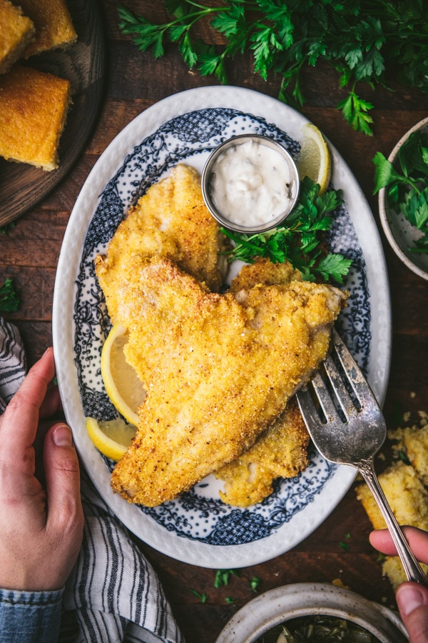 Hand served fried catfish from a blue and white plate.