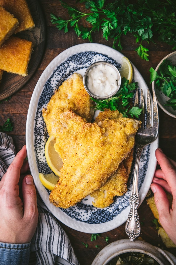 Hand holding a plate of crispy southern fried catfish.