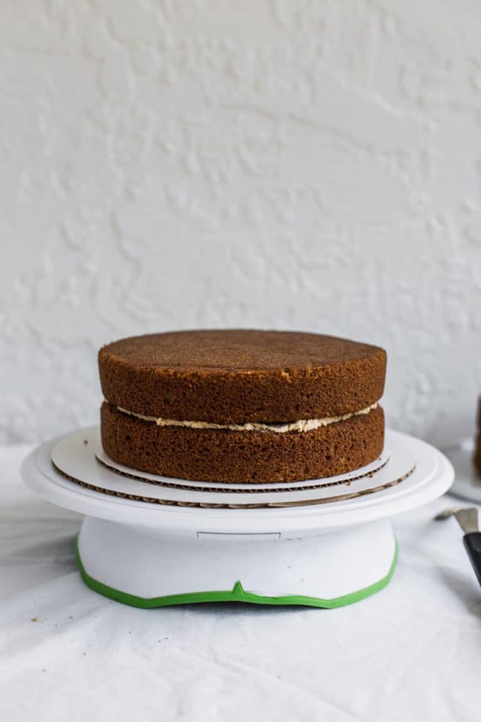 a beige cake sitting on a white and brown cake stand