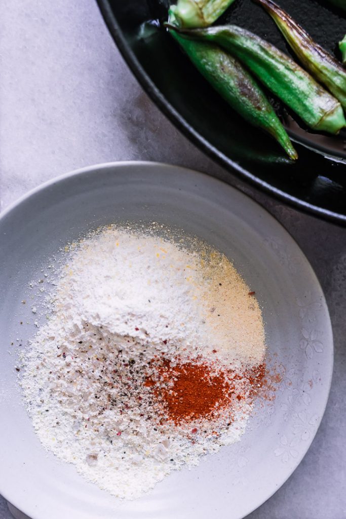 A bowl of cornmeal with paprkia and a cast iron skillet with okra.