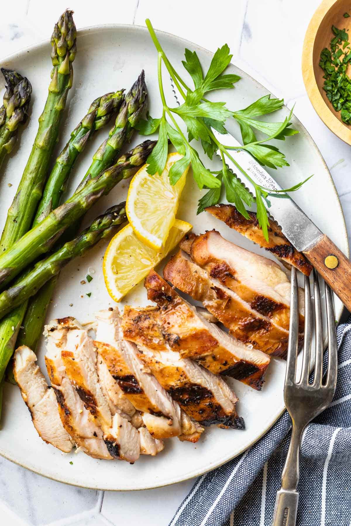 slice grilled chicken thighs on a plate with asparagus and two slices of lemon