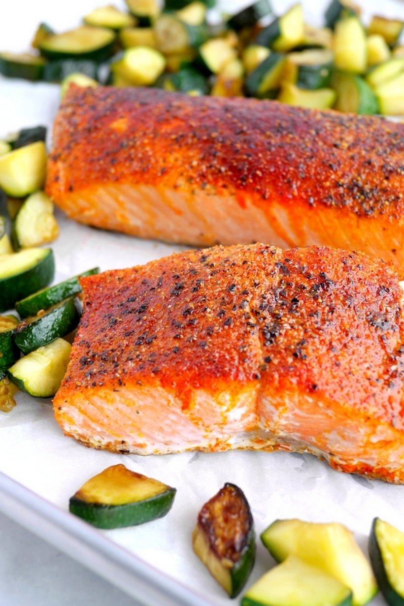 Two pieces of cooked salmon surrounded by vegetables.