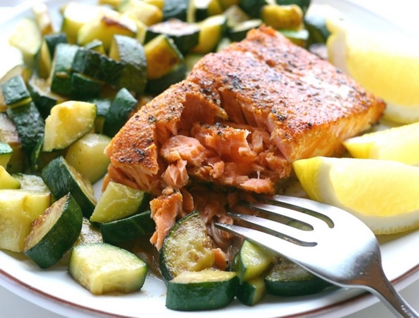Grilled salmon on a plate of zucchini with lemon slices and a fork.