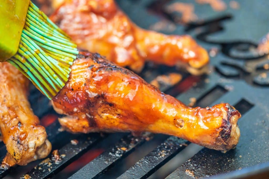 Chicken thighs on the grill are grilled with BBQ sauce by brush.