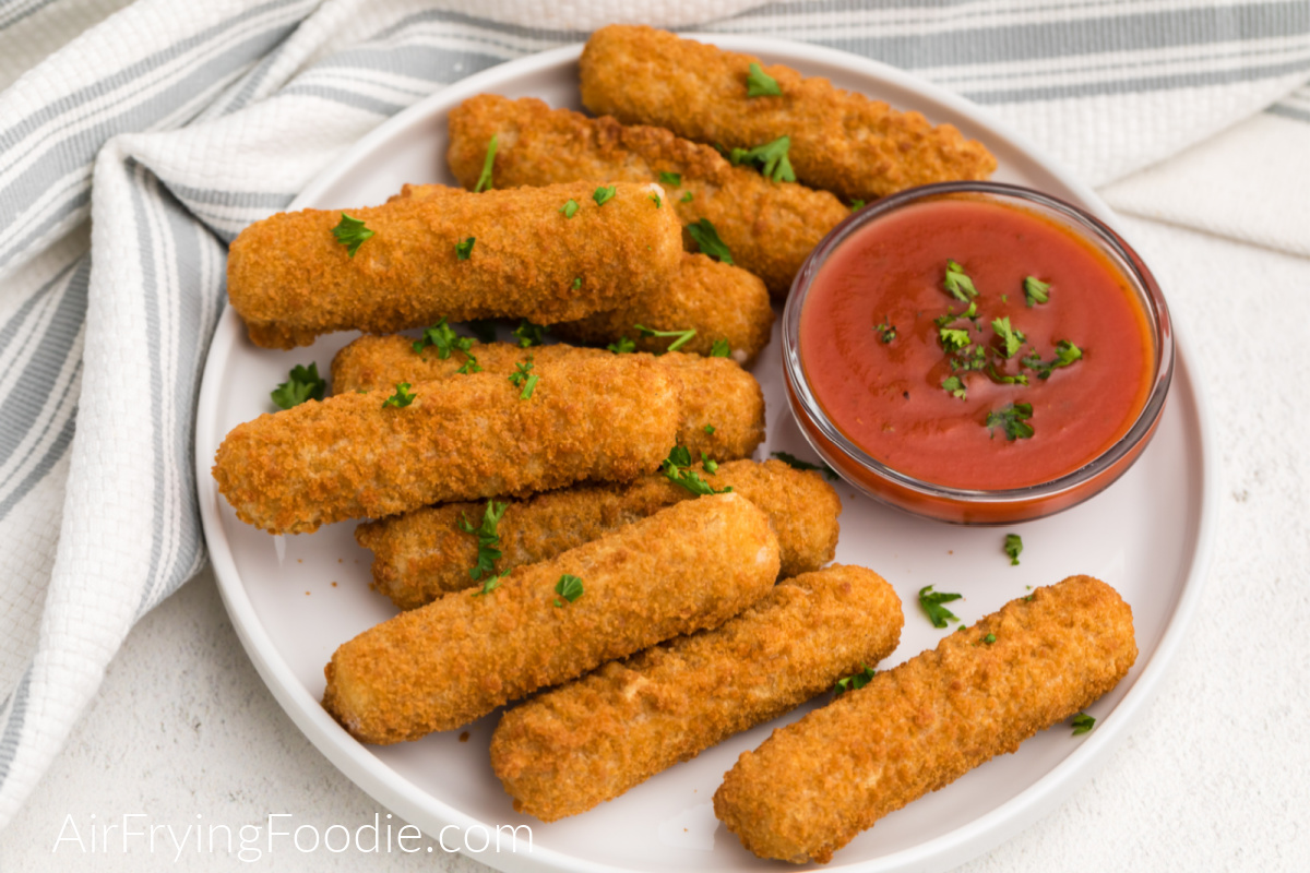 Mozzarella sticks are frozen and then air-fried - placed on a white plate and topped with fresh parsley.