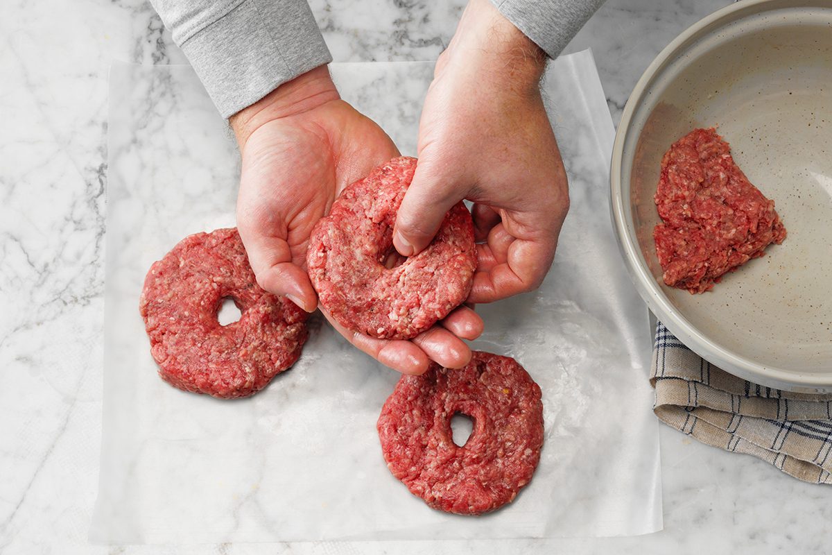Easy grilled burgers; How to; granite surface; overhead camera angle; granite surface; hamburgers; hamburgers; Hamburger; hamburgers; hands; preparation; in process; mixing bowl; ground beef; buds; spring rolls; wax paper; step #3 make a hole by hand in the center of the burger; raw beef; uncooked