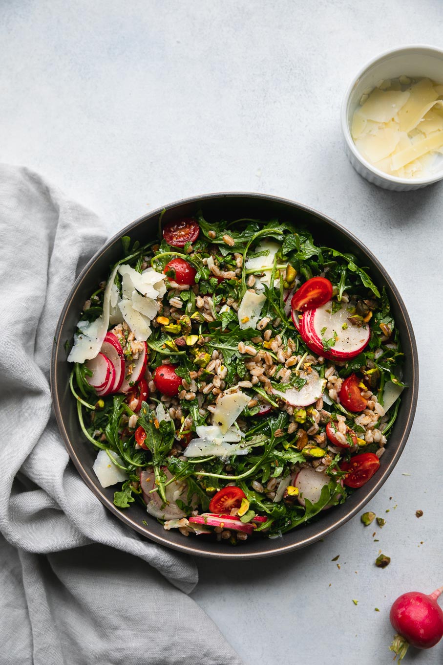 Aerial shot of arugula farro salad with tomatoes, sliced ​​radish, shredded parmesan and chopped pistachios