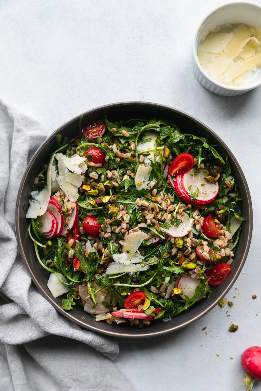 Aerial shot of arugula farro salad with tomatoes, sliced ​​radish, shredded parmesan and chopped pistachios