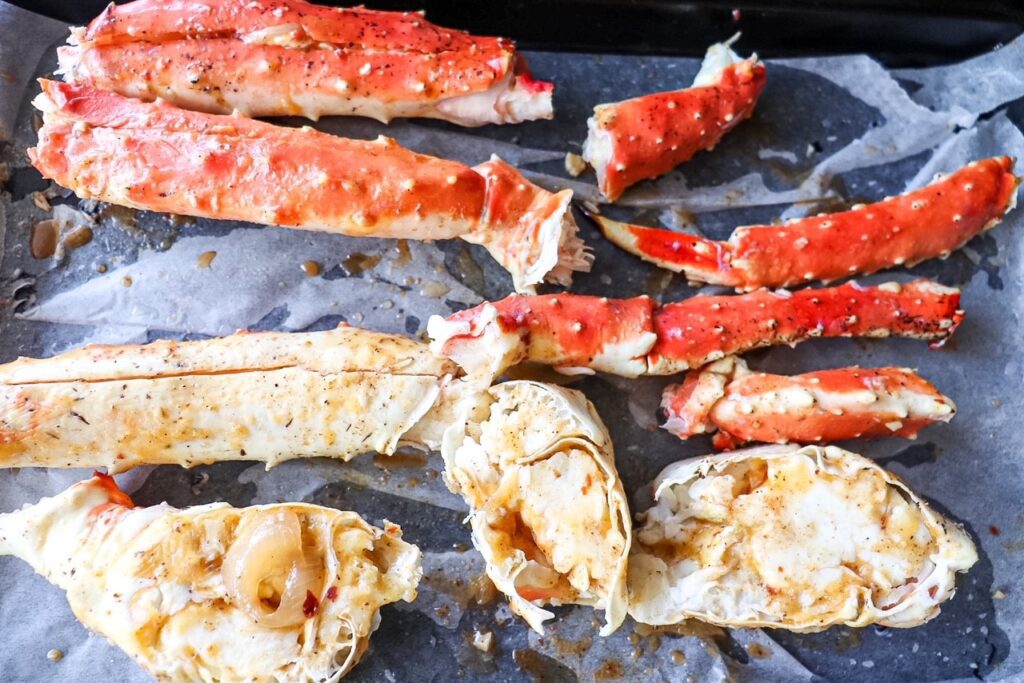 Split crab legs sitting on parchment-lined baking dish