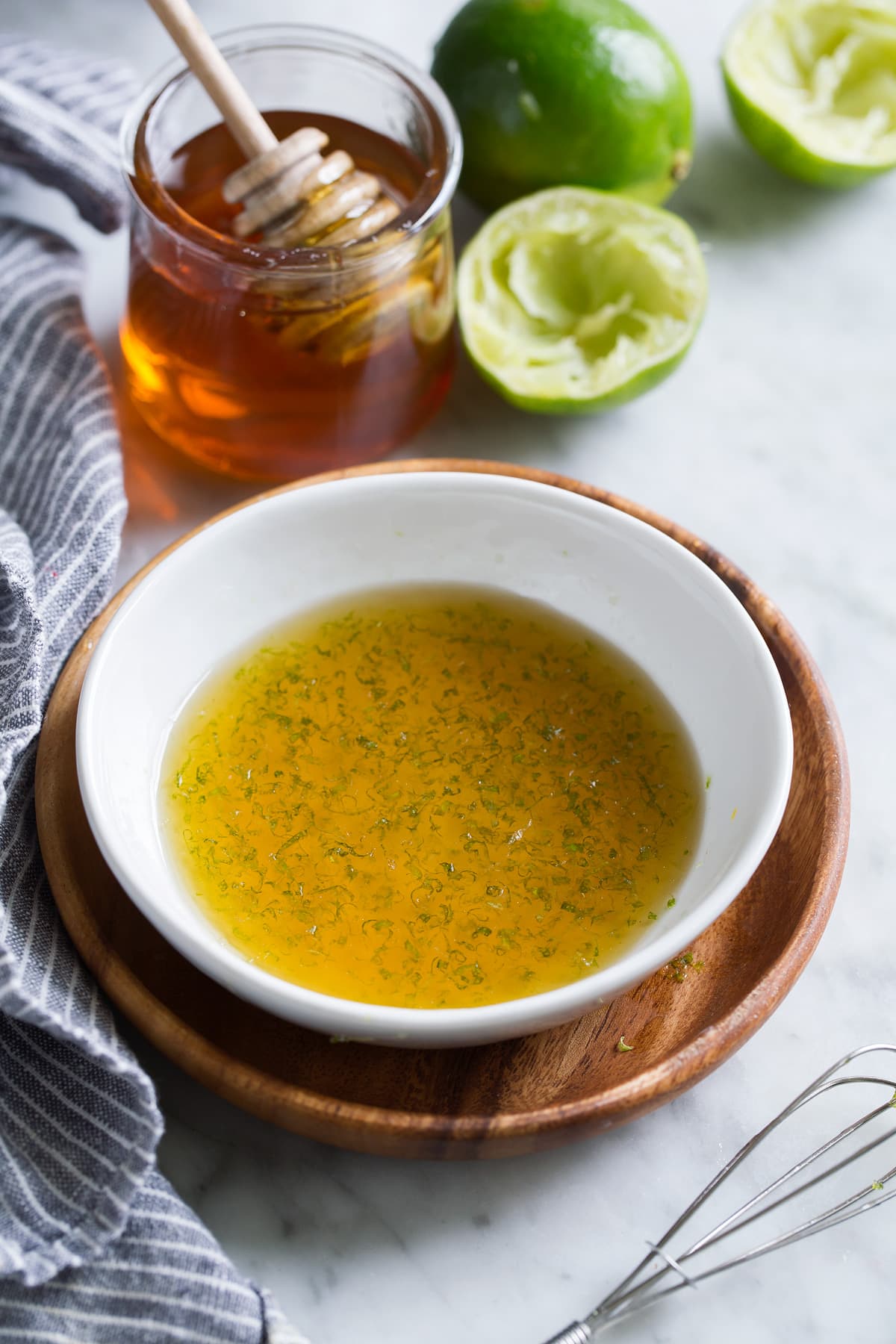 Honey lemon fruit salad dressing in a small white bowl set on a wooden plate.