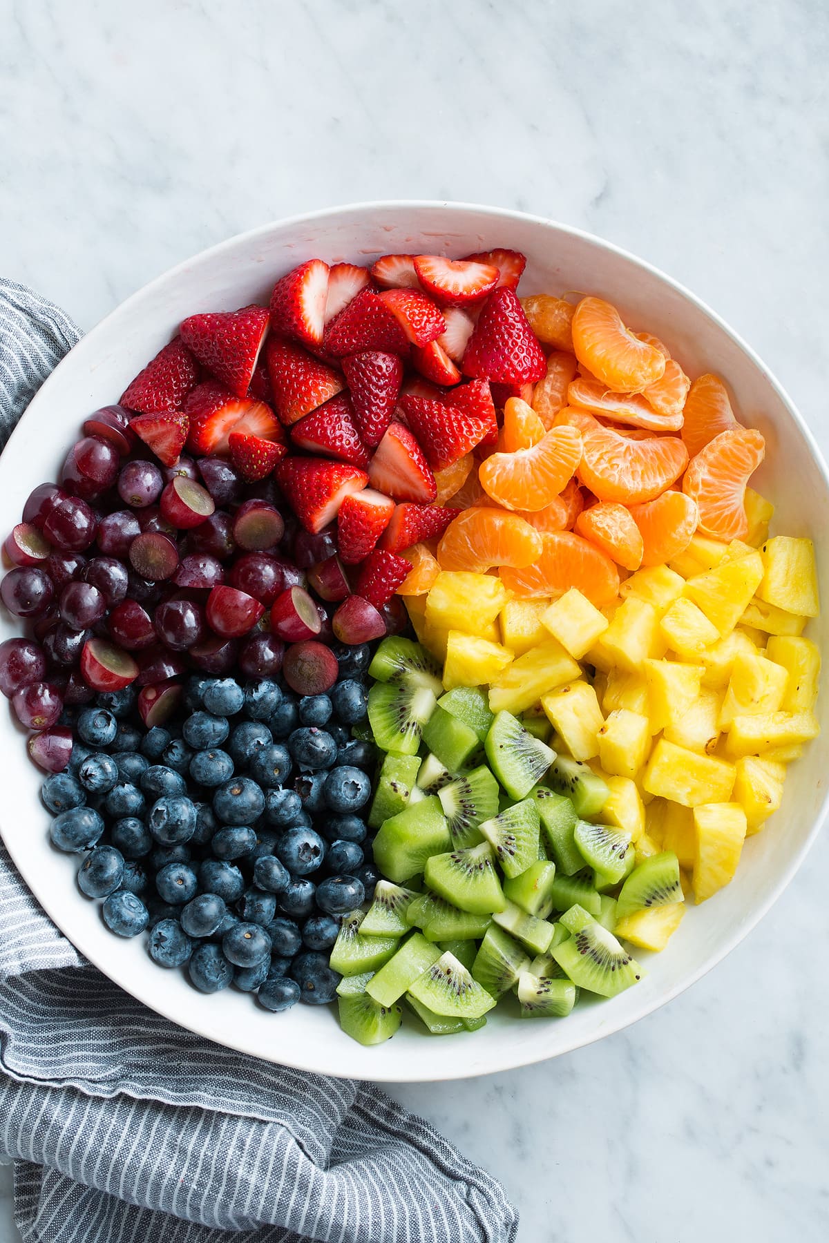 Fresh strawberries, citrus, pineapple, kiwi, blueberries and grapes in a large white bowl.