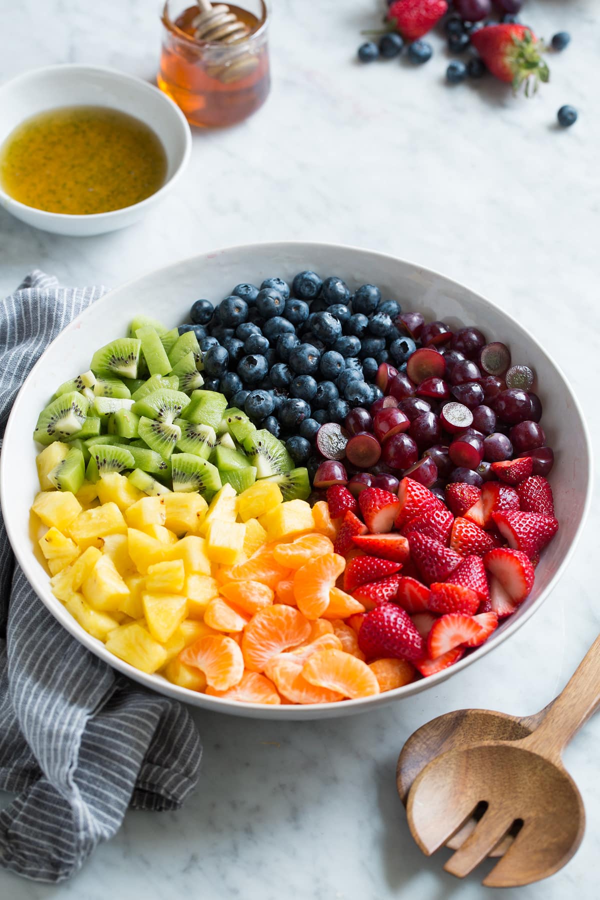 Fresh strawberries, citrus, pineapple, kiwi, blueberries and grapes in a large white bowl.