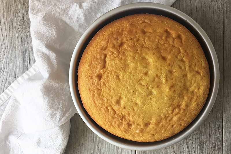 Horizontal image of baked yellow cake in a pan with a white napkin.