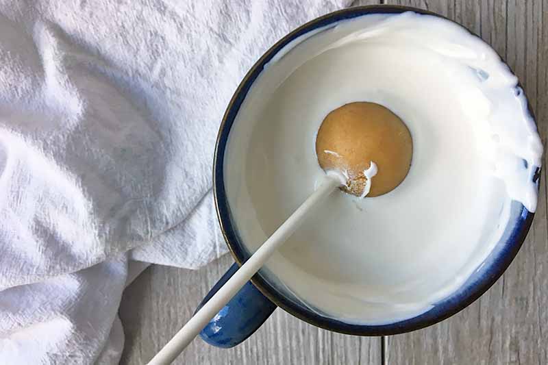 Dipping a cake ball in a mug filled with melted chocolate.