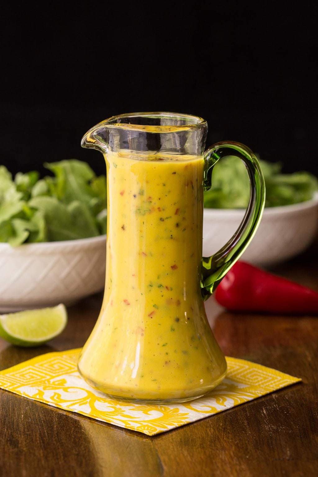 Image of a glass of Sweet and Spicy Mango Salad Garnished with bowls filled with salad in the background.