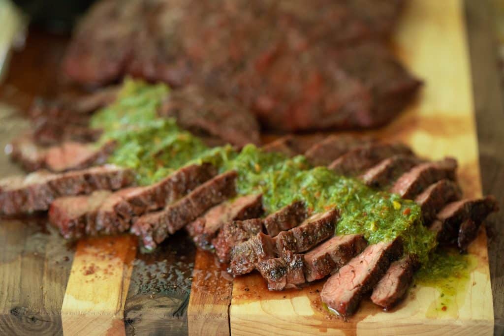 Slice steak with chimichurri on a wooden cutting board.